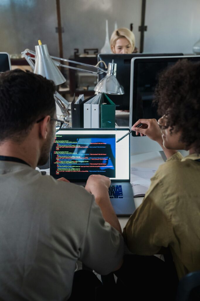 Two developers engage in software programming on a laptop in a modern office setting.